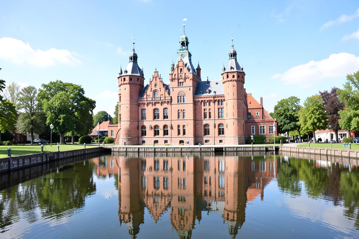 Backsteinschloss mit Türmen, gespiegelt im umgebenden Wassergraben