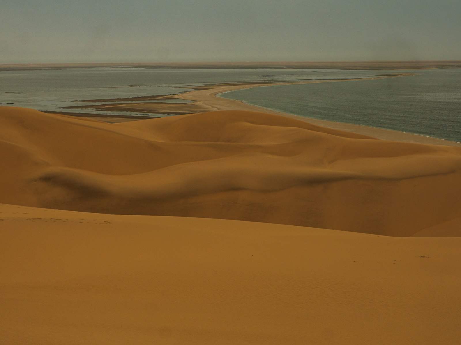 Weite Sanddünen treffen unter diesigem Himmel auf das Meer
