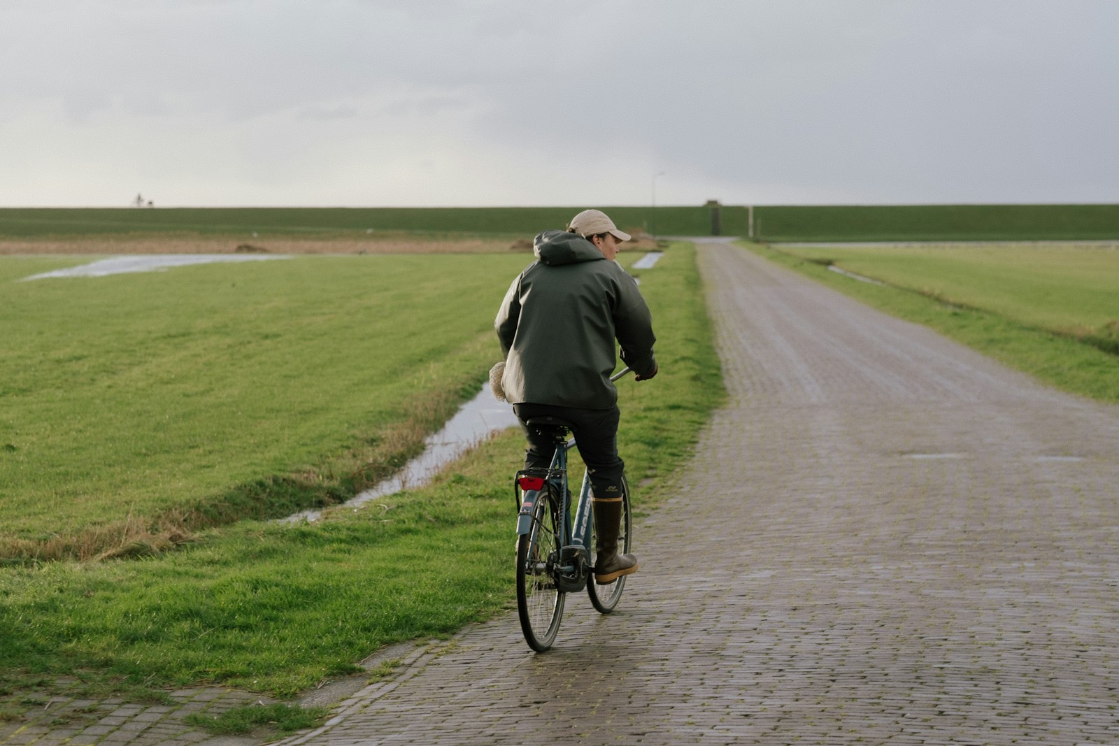 Radfahrer auf nasser Landstraße neben grünen Feldern