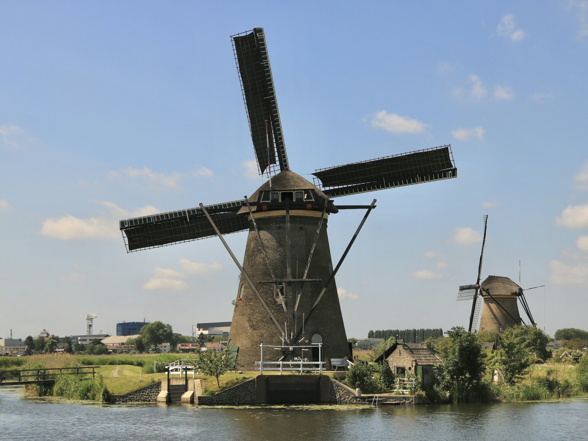 Windmühle an einem Wasserlauf vor grüner Wiese in den Niederlanden